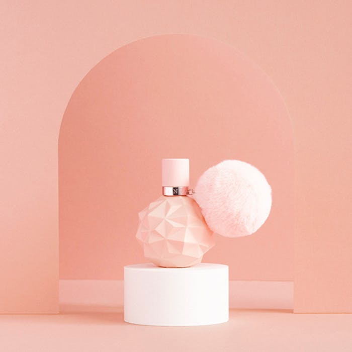 Pink perfume bottle with a matching pink sphere on a white pedestal against a pink background
