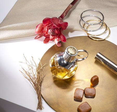 Perfume bottle, flowers, and candies on a gold plate with a white background