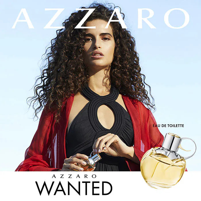 Azzaro Wanted perfume advertisement with a woman holding a perfume bottle against a clear blue sky.