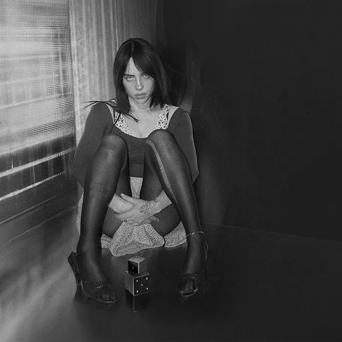 Black and white photo of a person sitting on a stool by a window.