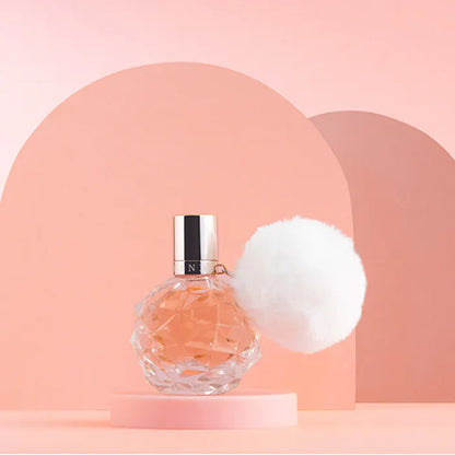 Perfume bottle with a white pom-pom on a pink background