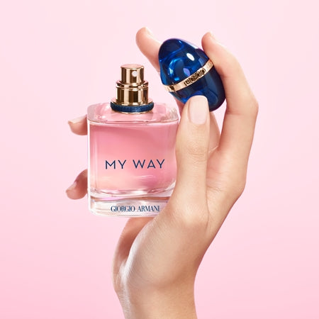 Hand holding a pink Giorgio perfume bottle labelled 'My Way' against a pink background