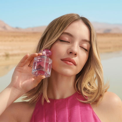 Woman in a pink dress holding a small glass bottle with a desert landscape in the background