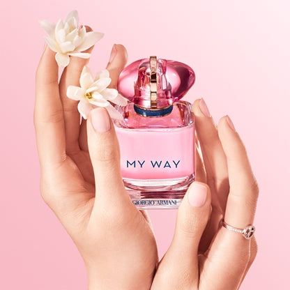Pink Giorgio perfume bottle held by a hand with flowers against a pink background