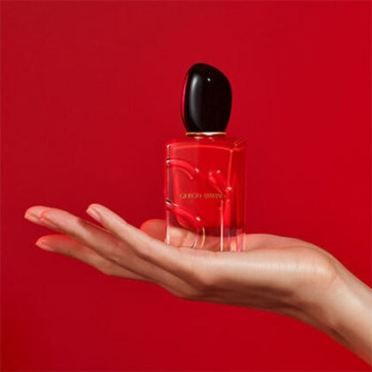 Red perfume bottle with black cap held in a hand against a red background