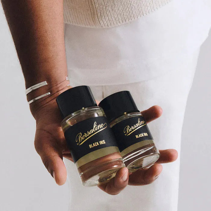 Two perfume bottles held by a person against a plain background